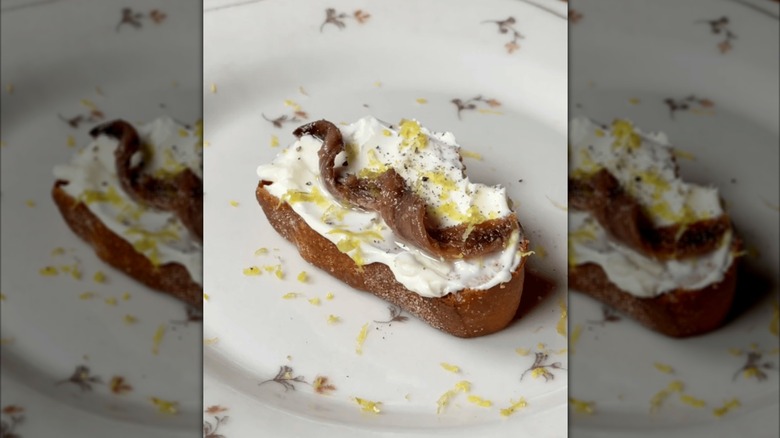 Toast with anchovy, vodka butter, and lemon zest on a white floral-patterned plate