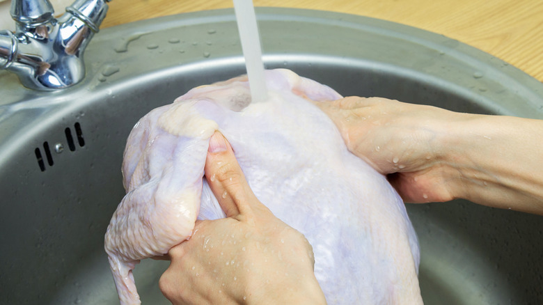 A person washes a whole chicken in a sink.