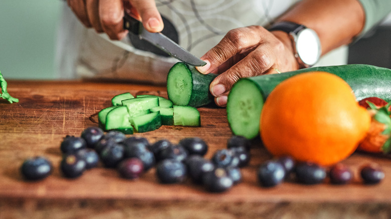 Chopping a cucumber with blueberries on a cutting board