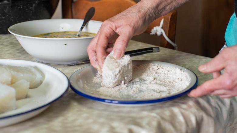 Hands dredging fish in flour