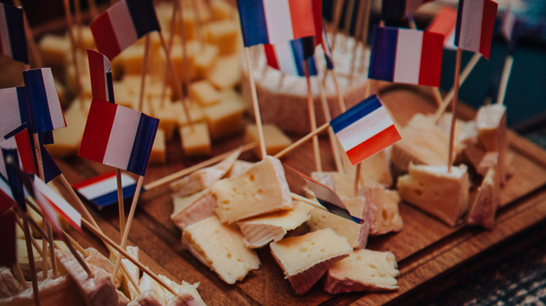 A display of various small bites of cheeses with miniature French flags on toothpicks sticking out of the cheeses