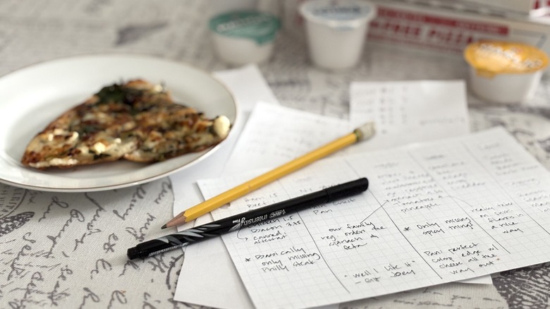 scorecards with writing implements next to plate with Domino's pizza