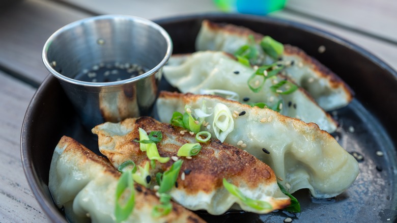 Gyozas topped with scallions with dipping sauce on the side