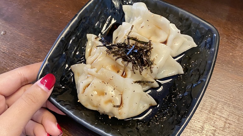 Woman's hand holding plate of gyoza topped with seaweed