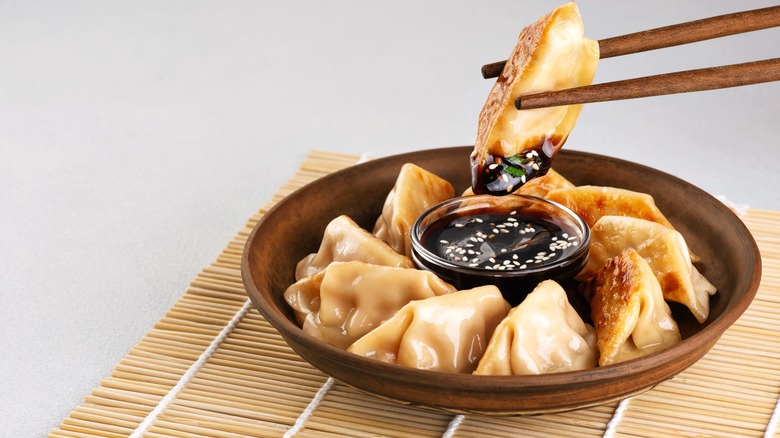 Chopsticks holding gyoza over bowl of dipping sauce