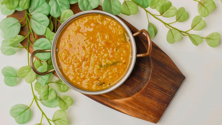 A pot full of moong dal curry on a wooden cutting board