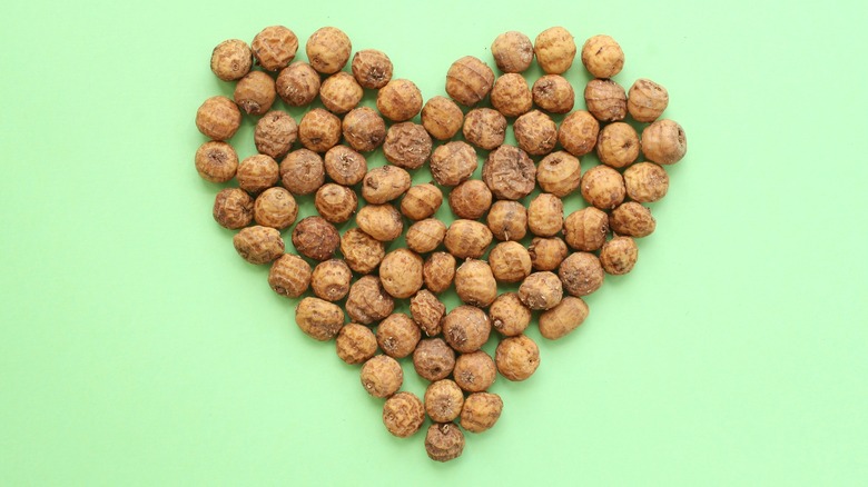 Whole tiger nuts are arranged in a heart on a green background