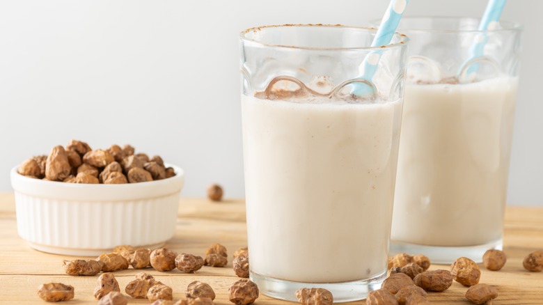 Two glasses of horchata de chufa with blue and white polka dot straws sit next to a white bowl of tiger nuts on a wooden table