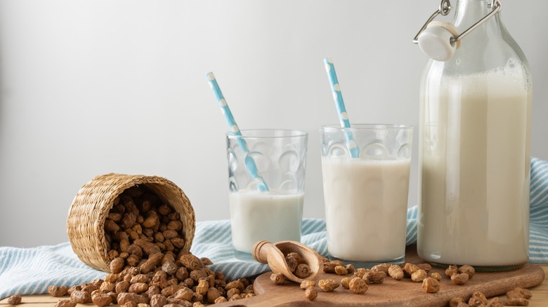 A jar of horchata de chufa with two glasses and an overturned basket of tiger nuts