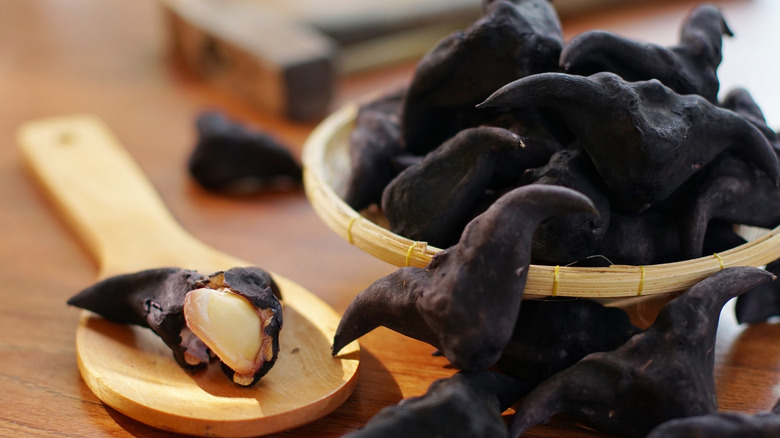 Water caltrop pods in a bowl with one opened pod on a wooden spoon