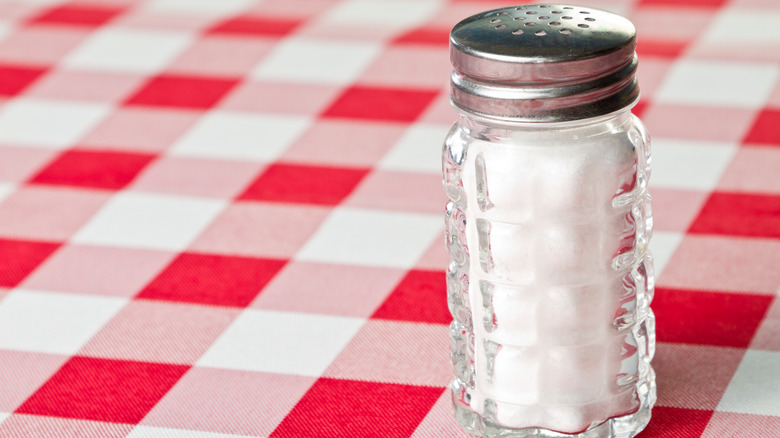 A salt shaker on a red-checked tablecloth.