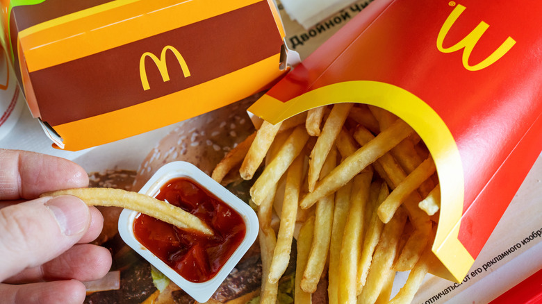 A hand dips a McDonald's french fry, from an overflowing container, into a small tub of ketchup