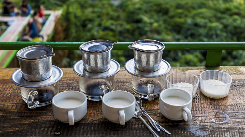 Three Vietnamese phins brewing coffee next to mugs of condensed milk