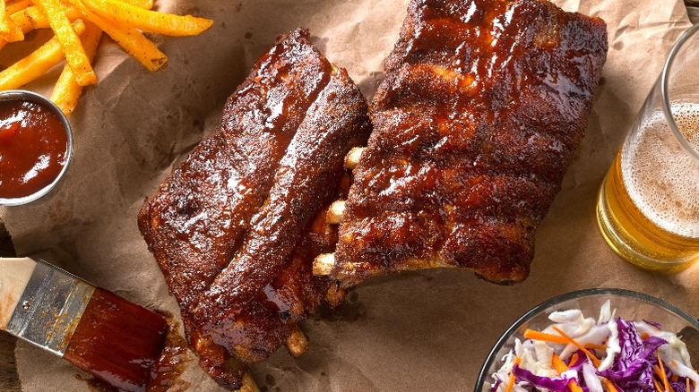 Ribs and barbecue sauce are spread out on paper with sides and a drink.