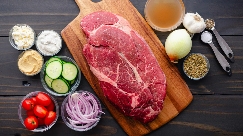 Raw chuck roast on a cutting board with vegetables