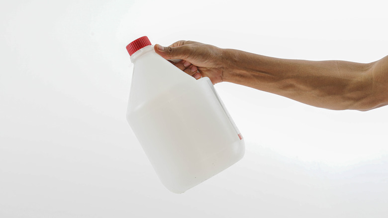 Person holding a plastic jug with a red lid