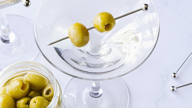 A martini served up with two olives speared through a metal toothpick