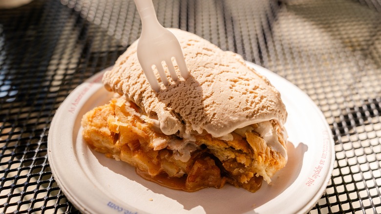 Slice of apple pie topped with ice cream and a fork