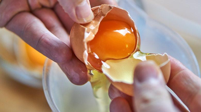 Person cracking egg with orange yolk