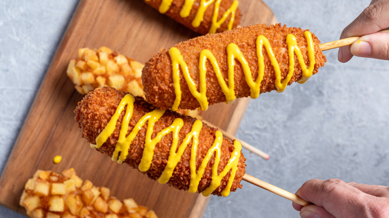 Hands holding corn dogs with mustard