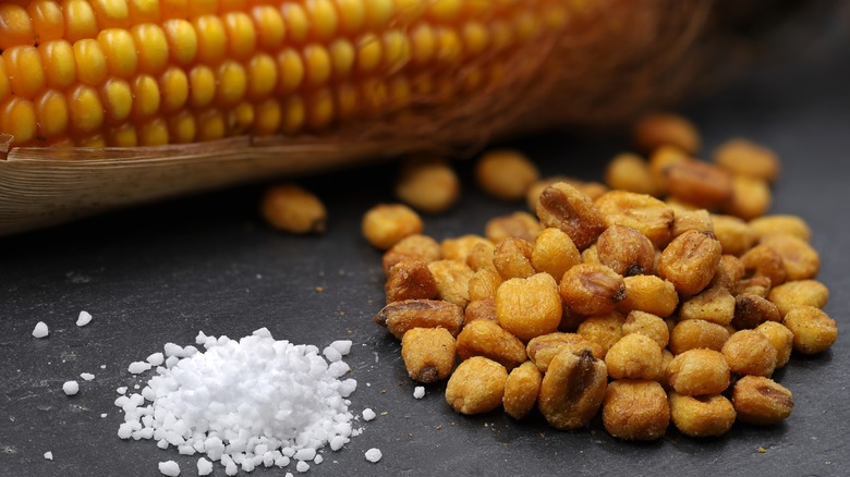 A husk of corn, fried corn kernels, and a pile of salt sit on a table