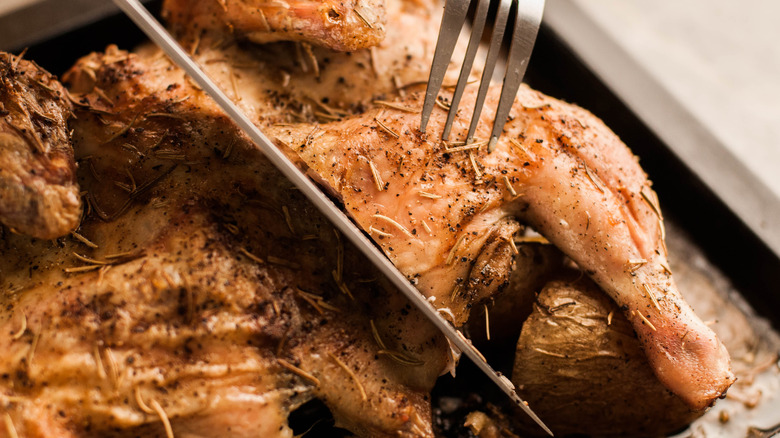 Cutting into a roasted chicken seasoned with herbs