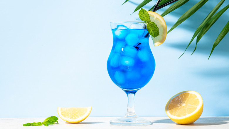 A blue lagoon cocktail on a blue background with citrus slices.