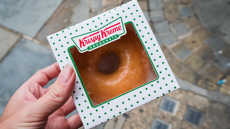 Person holding a box with a single Krispy Kreme glazed donut