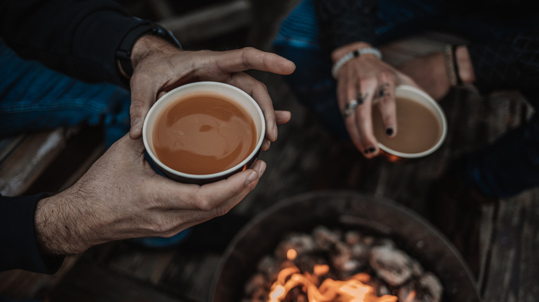 People holding mugs of kava over fire