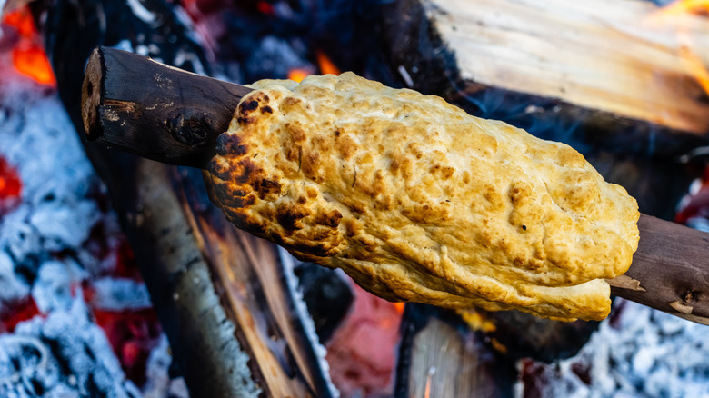 Bannock being cooked on a stick over a fire