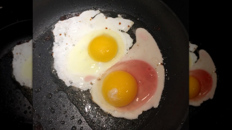 Two eggs in frying pan. One is a typical color and the other is a translucent pink color. 