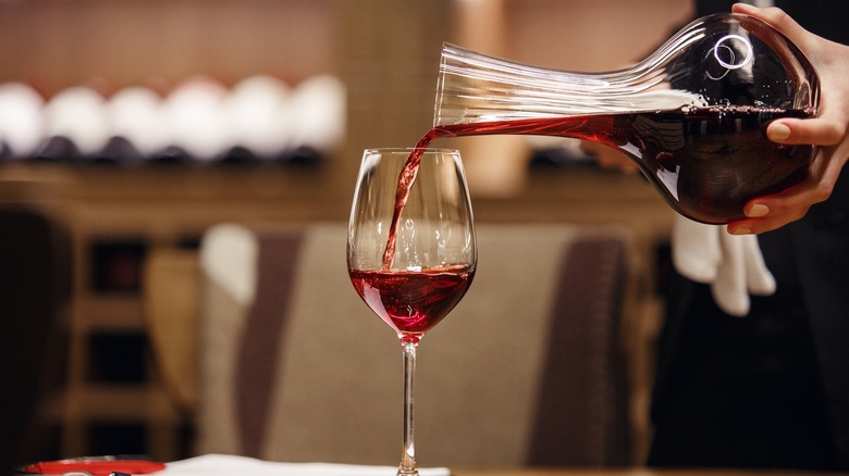 Sommelier pouring red wine into a glass from a decanter