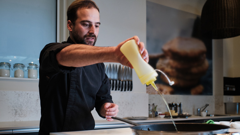 chef pouring oil from a bottle into a pan for cooking