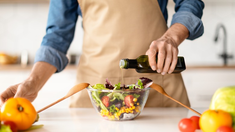 person in tan apron pouring oil onto a salad