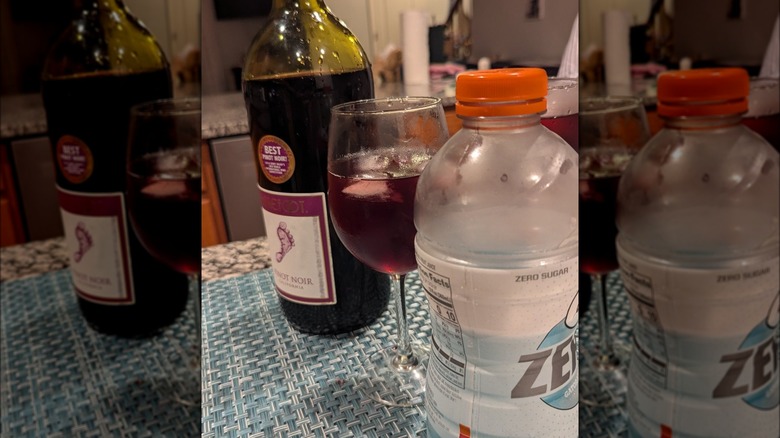 Glass of gatorwine between red wine and Gatorade bottles