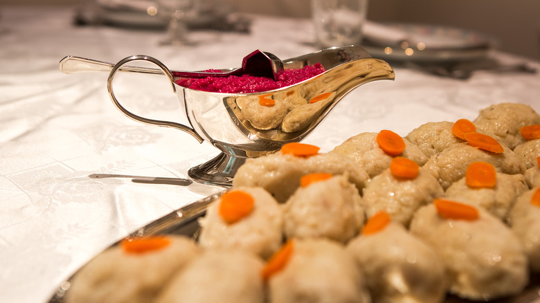 Balls of gefilte fish topped with carrots on a platter with a tureen of horseradish beside it