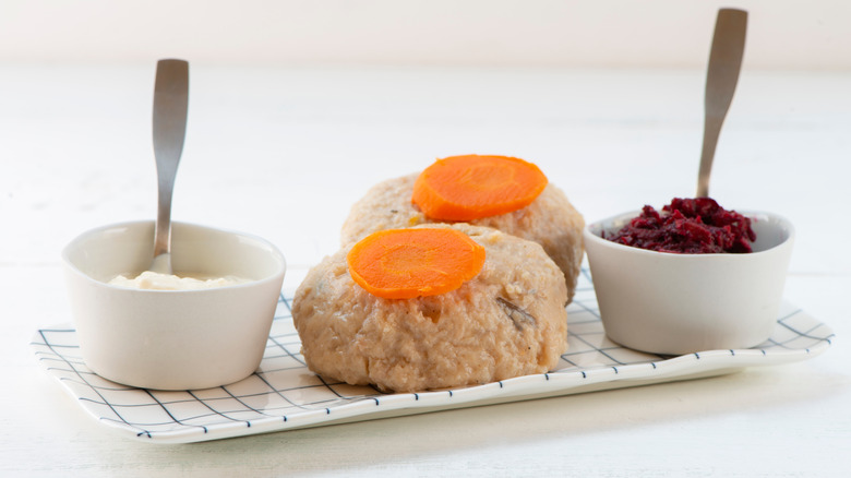 Two gefilte fish balls with carrots surrounded by a ramekin of mayonnaise on one side and a ramekin of horseradish on the other