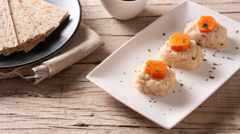 Gefilte fish balls with carrots sprinkled with herbs in a square dish, with a dish of matzo beside them