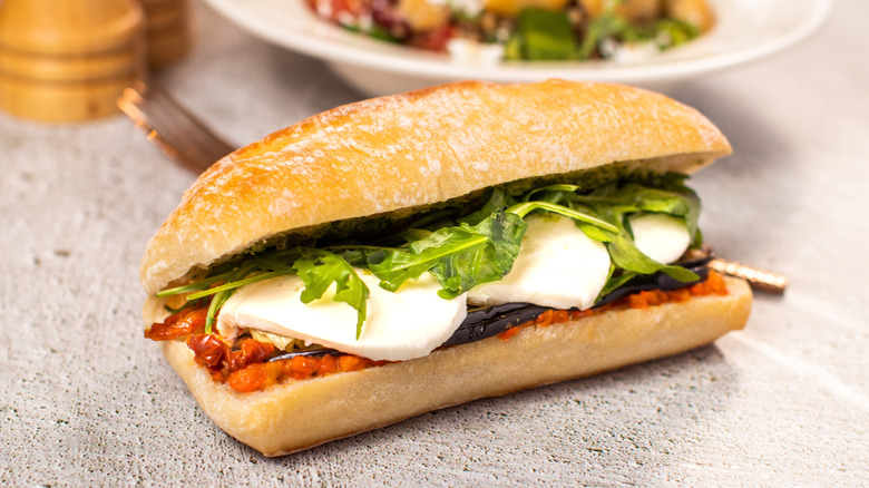 Halloumi and vegetables are served on a roll placed on a textured pink tabletop.