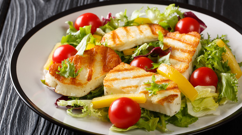 Grilled slices of halloumi top a colorful salad on a plate.