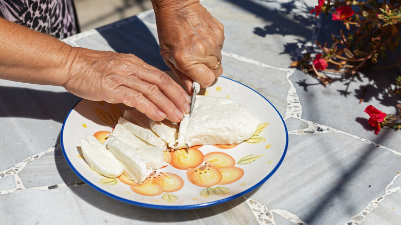 A woman from a village in Cyprus slices halloumi on a colorful plate.