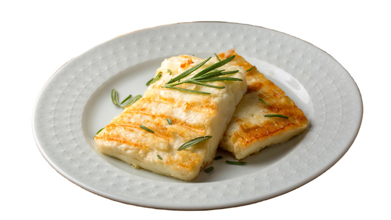 Grilled halloumi cheese slices are served on a white plate with rosemary leaves.