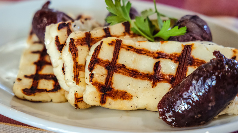 Grilled halloumi and sausages are served on a white plate.