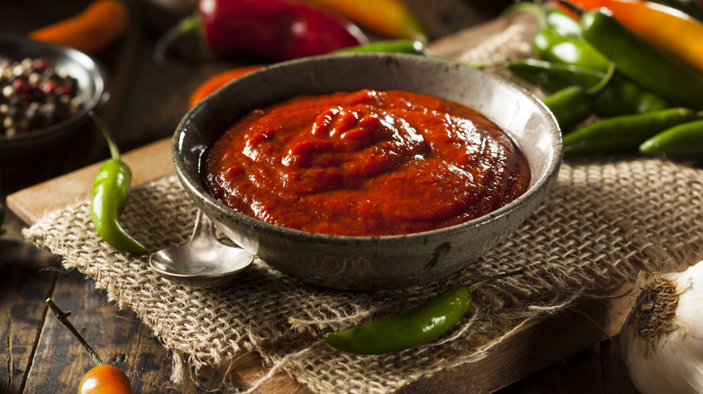Sriracha sauce in a bowl surrounded by red and green peppers