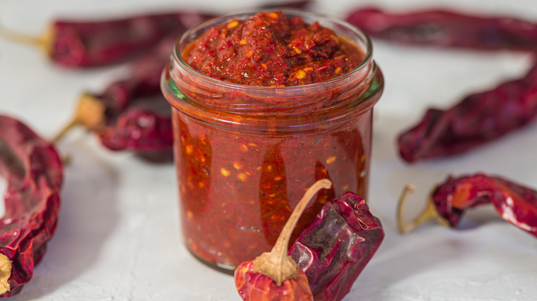 Harissa in a jar surrounded by red peppers