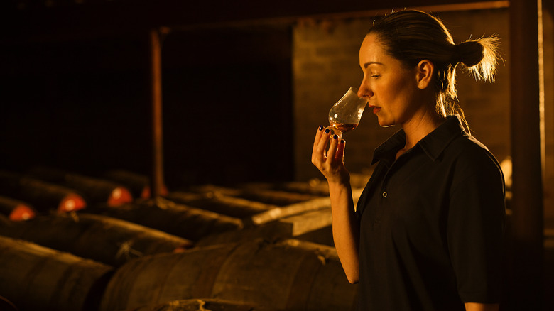 Woman nosing whiskey in barrel house