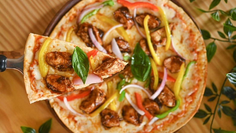 Slice of tikka chicken pizza over full pizza on wooden table