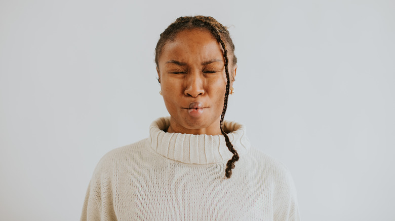 woman in white sweater puckers face with closed eyes