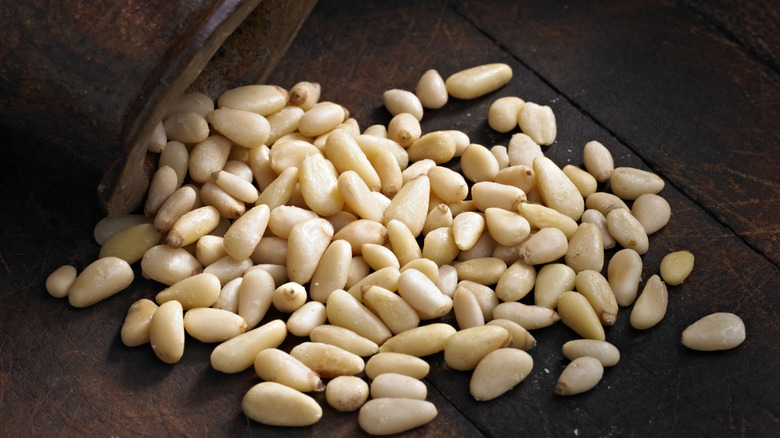 pine nuts spilling out of a jar onto dark wooden table