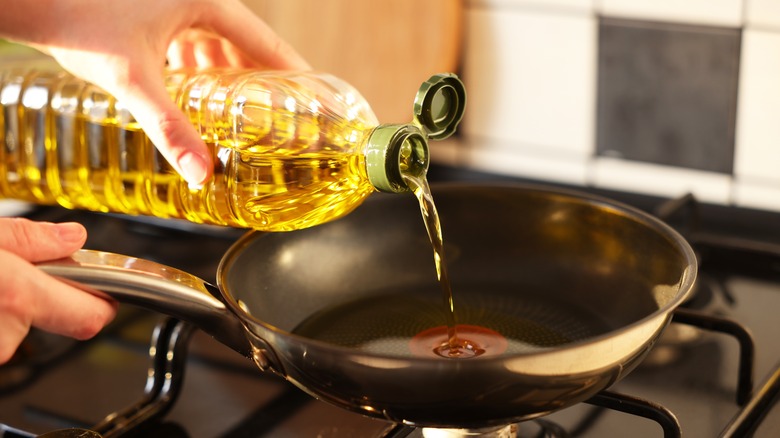 Pouring cooking oil into pan over stove burner